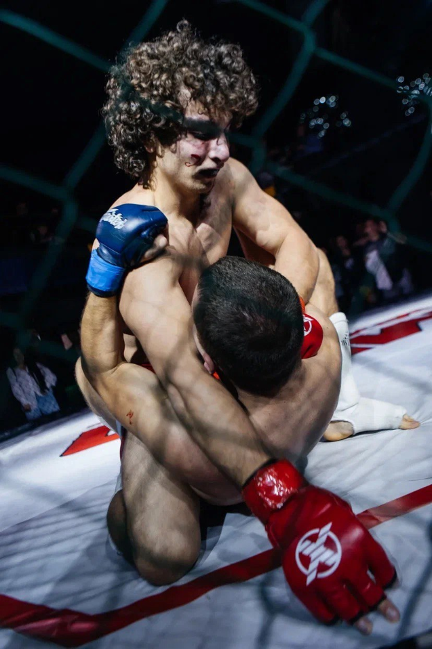 Zwei Männer in einem MMA-Ring im Kampf, wobei einer einen Tritt auf den anderen ausführt.