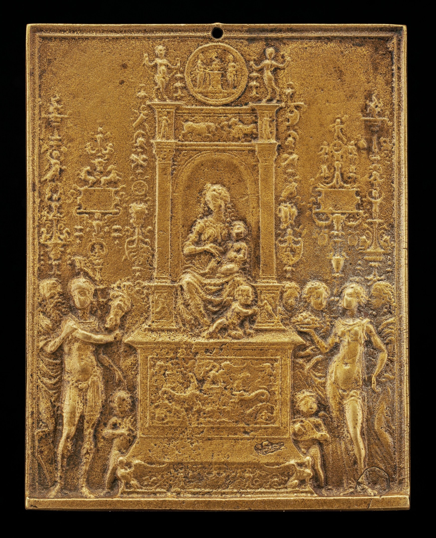 Goldene Plakette mit detaillierter Skulptur einer Frau in einem langen Kleid und eines Mannes in Anzug und Krawatte, eingerahmt von einem goldenen Rand, vor schwarzem Hintergrund.