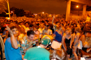 Menschen tanzen im Vordergrund eines Konzerts mit Lichtern, Polen, Bäumen und anderen Objekten im Hintergrund.