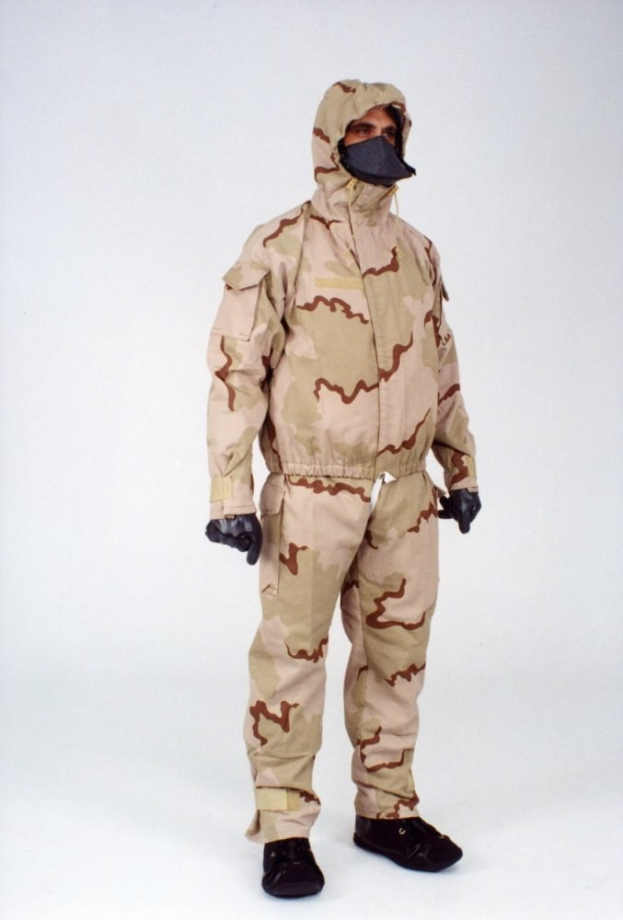 Mann in einem camouflagegemusterten Schutzoverall und Maske vor einem weißen Hintergrund.