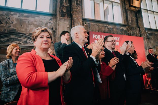 Eine Gruppe von Menschen, die vor einer Menge jubeln, mit einem Banner im Hintergrund, auf dem steht: "Wir haben die Wahl gewonnen."