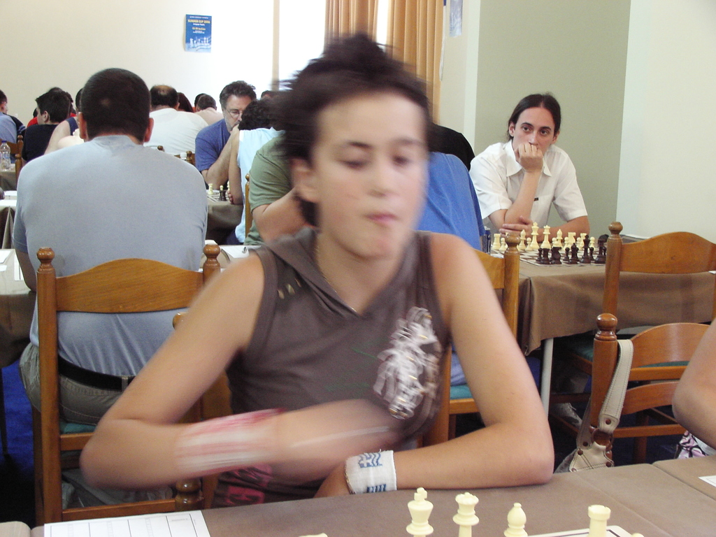 Ein Raum mit Menschen an Tischen sitzend, die Schach spielen, mit einer Vorhangwand und einem Foto in der Ecke.