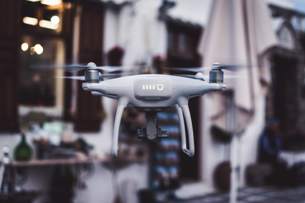Weißer DJI Phantom 3 Advanced Drohne im Flug gegen einen unscharfen Hintergrund von Gebäuden und Lichtern.