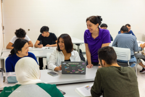 Eine Gruppe von Menschen in einem Klassenzimmer, die um einen Tisch mit Laptops, Büchern und anderen Gegenständen sitzen und über Klimawandel diskutieren, wie es im Bildtitel "Wake Tech: Ein Leitfaden zum Klimawandel" angegeben ist.