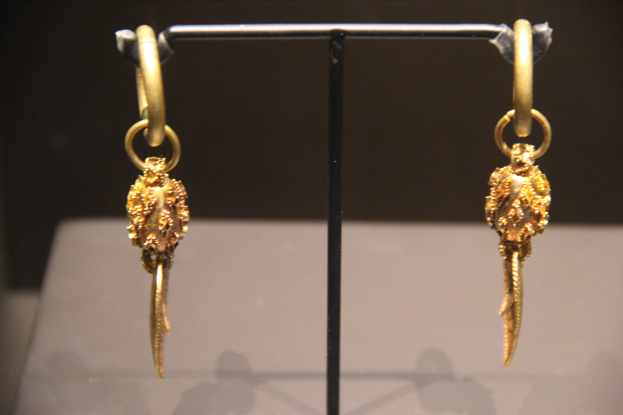 Goldene Ohrringe auf einem Ständer in einer Glasvitrine mit unscharfem Hintergrund.