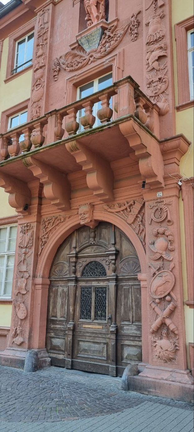 Altes Gebäude in der Heidelberger Altstadt mit einer hölzernen Tür, Fenstern und kunstvollen Fassadenverzierungen.