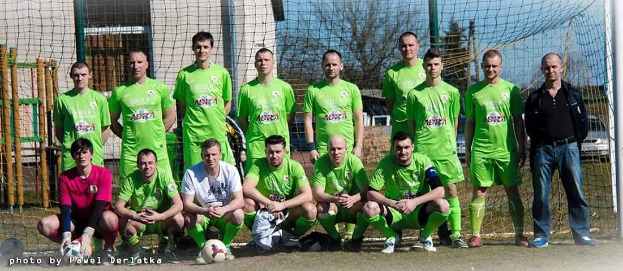 Gruppe von Männern in grünen T-Shirts, die auf einem Fuballfeld mit einem Ball und einem Torpfosten im Hintergrund stehen.