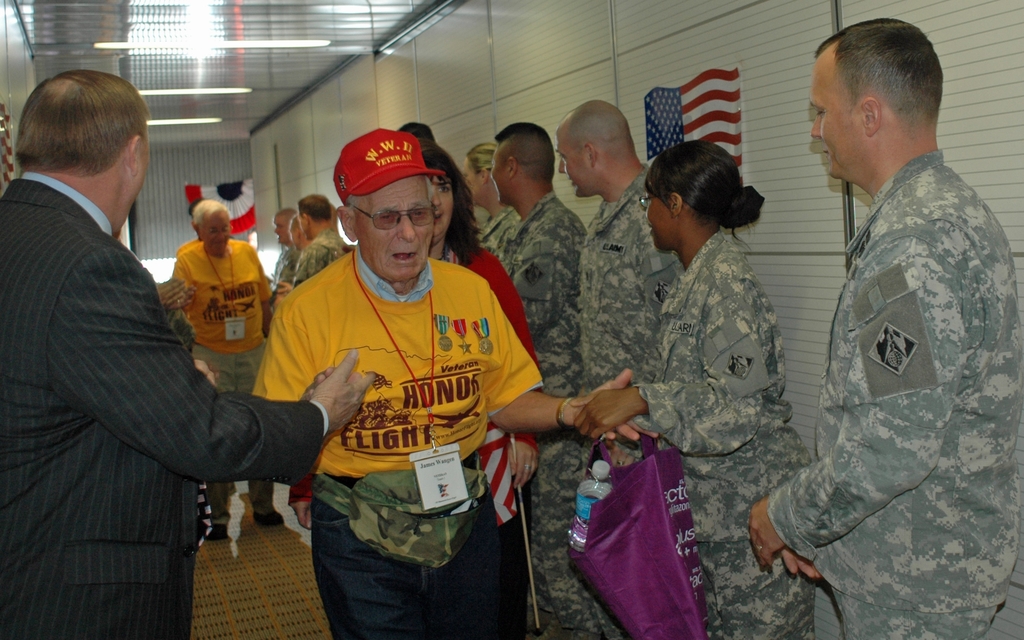 Eine Gruppe von Menschen und Soldaten, die drinnen stehen, mit einer Flagge an der rechten Wand und Lampen an der Decke.