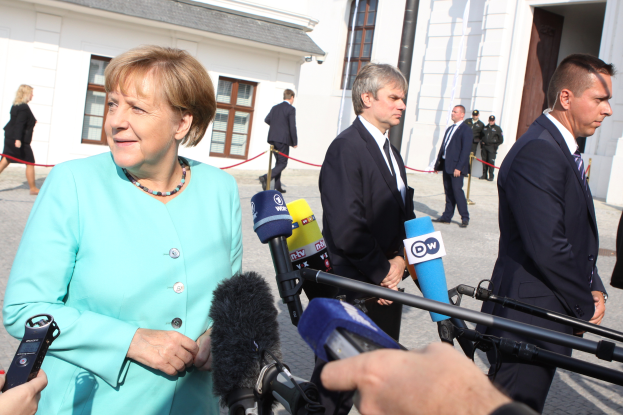 Bundeskanzlerin Angela Merkel spricht zu Reportern vor dem Kanzleramt in Berlin, umgeben von einer Gruppe von Menschen, einige halten Mikrofone, mit Gebäuden im Hintergrund.