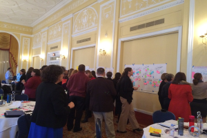 Eine Gruppe von Menschen untersucht Plakate und Charts, die an einer Wand in einem Raum zu sein scheinen, der wie ein Kunstmuseum aussieht.