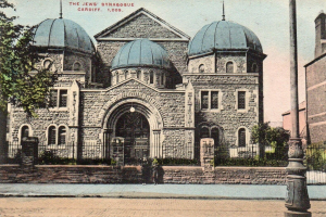 Eine alte Postkarte zeigt die jüdische Synagoge in Cardiff, Ontario, Kanada, mit einem Gebäude mit Fenstern, Türen und Bögen, umgeben von Pflanzen, einem Zaun, Bäumen, einem Pfahl und einem bewölkten Himmel, mit Text oben.