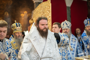Eine Gruppe von Männern mit Kronen steht zusammen in einer Kirche, mit einem Patriarchen in der Mitte, einer Wand und einer Säule im Hintergrund und Text mit einem Logo unten.