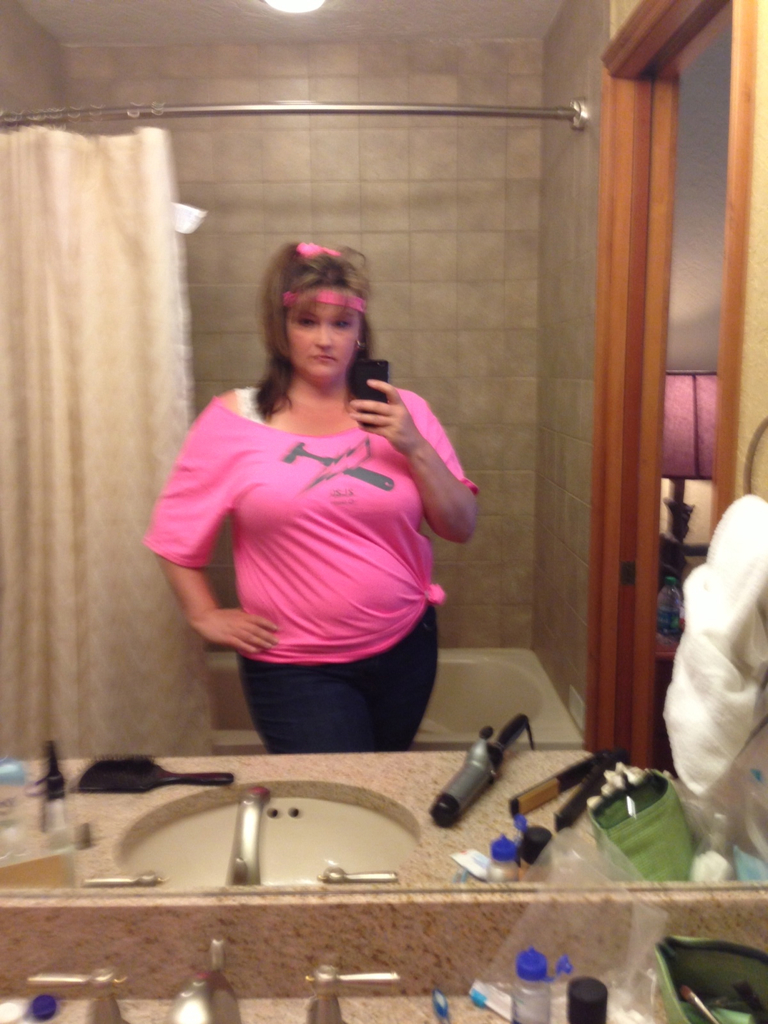 Eine Frau in einem rosafarbenen T-Shirt macht ein Selfie in einem Badezimmerspiegel mit Blick auf das Meer.