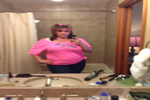 Eine Frau in einem rosafarbenen T-Shirt macht ein Selfie in einem Badezimmerspiegel mit Blick auf das Meer.