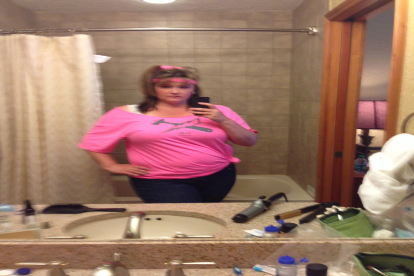 Eine Frau in einem rosafarbenen T-Shirt macht ein Selfie in einem Badezimmerspiegel mit Blick auf das Meer.