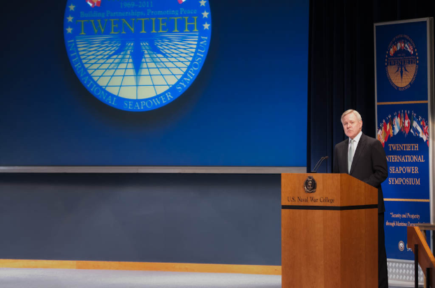 US-Außenminister Mike Pompeo, in einem schwarzen Blazer, weißem Hemd und schwarzer Krawatte, steht an einem Podium mit zwei Mikrofonen und spricht bei der 20. Internationalen Seapower Symposium, mit einem blauen Bildschirm und Geländer rechts.