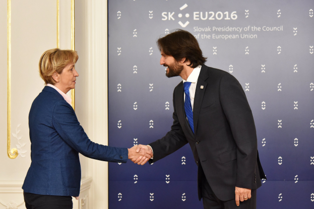 Bundeskanzlerin Angela Merkel und Bundeskanzlerin Joachim Gauck schütteln sich die Hände vor einer Wand mit einem "EU-Gipfel"-Banner und einer Tür im Hintergrund, beide lächeln.