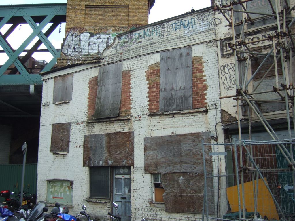 Ein Hausgebilde in der Mitte, mit Fahrzeugen unten, einem Pfahl links, einer Brücke oben und einer hölzernen Bambusstruktur rechts.