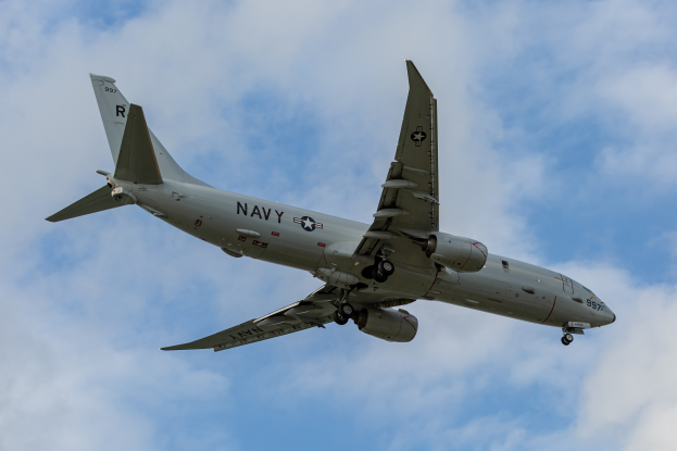 Ein großes Militärflugzeug mit Text und Zahlen, die darauf hinweisen, dass es eine Joint Direct Attack Munition ist, fliegt durch einen blauen Himmel mit weißen, flauschigen Wolken.