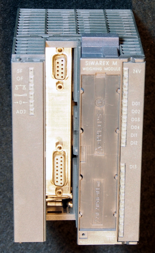 Nahaufnahme eines silbern glänzenden, rechteckigen elektronischen Geräts auf einem Tisch, das Ports an der Vorderseite und Knöpfe an der Seite aufweist.