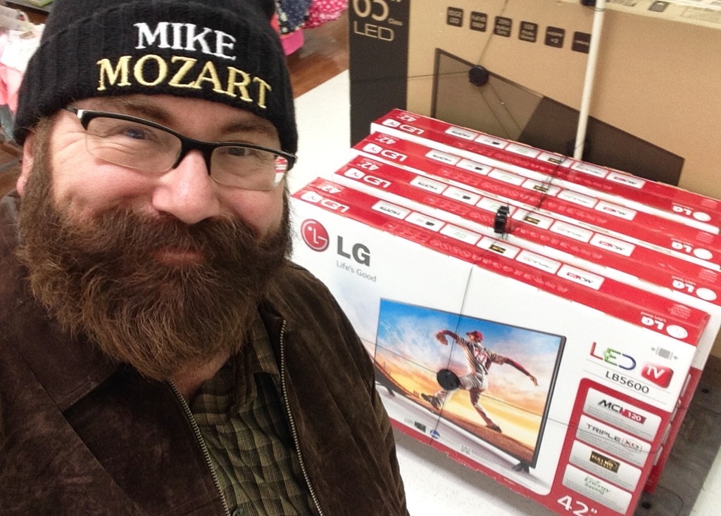 Eine Person, die vor Fernsehgeräten in Kartons und anderen Gegenständen lächelt.