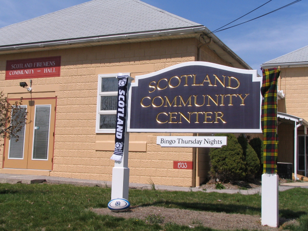 Außenansicht des Scotland Community Center mit einem Schild, Gras, einem Ball, Pflanzen, einem Baum, Drähten und einem bewölkten Himmel.