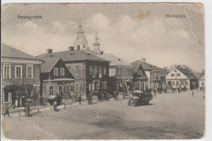 Ein altes Schwarz-Weiß-Foto einer Stadtstraße in Nowogrodeek, Deutschland, das Gebäude, Menschen, Karren, Pfähle und Bäume zeigt, mit der Aufschrift "Marktplatz in Nowogrodeek, Deutschland" oben und unten.
