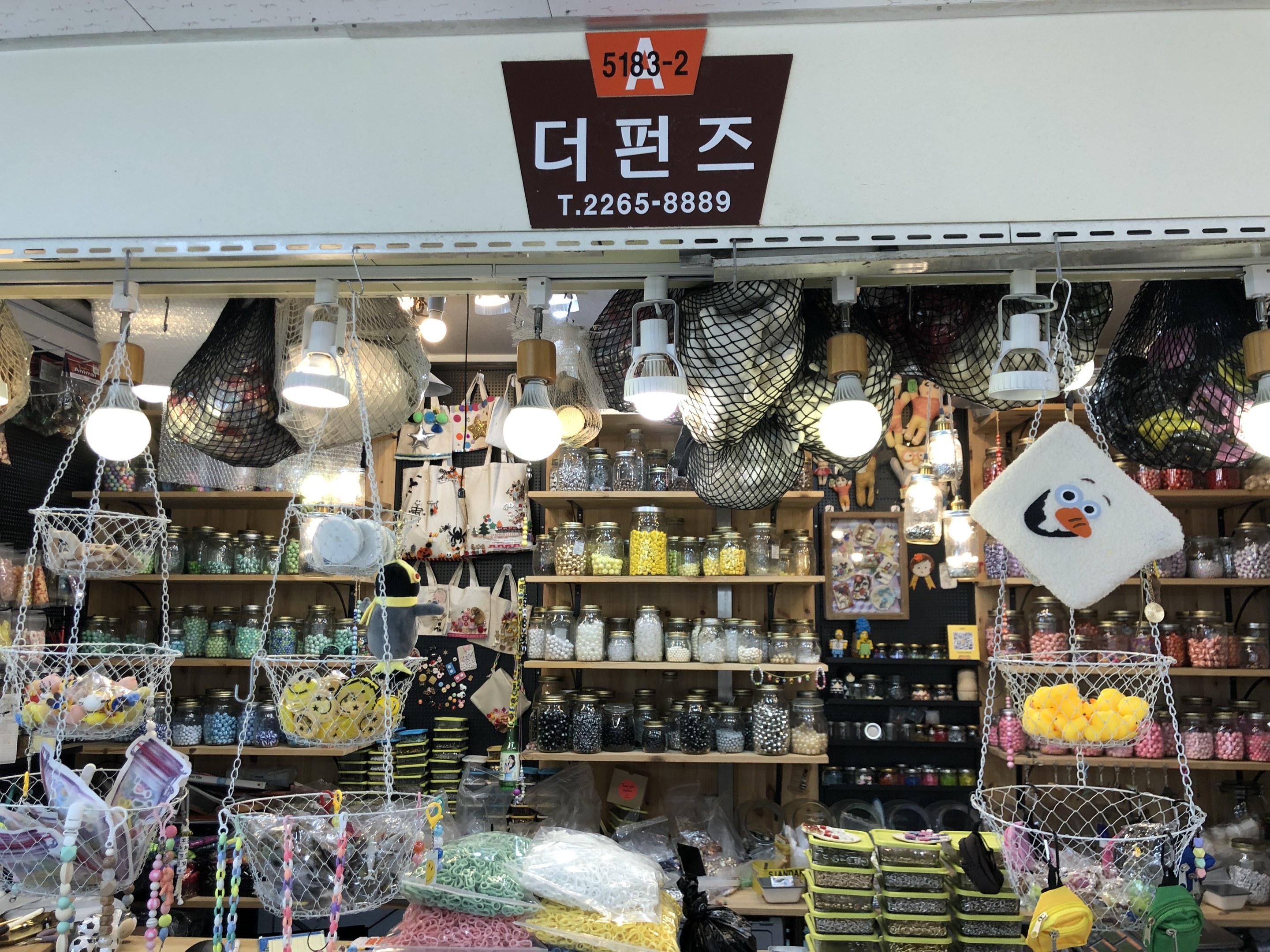 Ein unordentlicher Laden in Seoul mit verschiedenen Artikeln wie K%C3%B6rbchen, Lichtern, Flaschen und Spielzeugen auf Regalen, mit einer Tafel oben, die ihn als einen der besten koreanischen L%C3%A4den kennzeichnet.