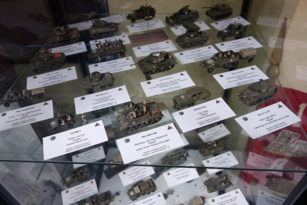 Vitrine mit verschiedenen Militärfahrzeugen, einschließlich Panzern, auf einem Glastisch, begleitet von informativen Papieren.