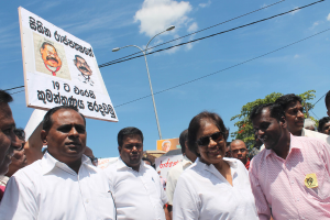 Männer stehen und protestieren, halten Schilder, mit Polen, Drähten, Bäumen und dem Himmel im Hintergrund.
