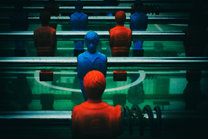 Ein buntfarbiger Tischfußballtisch mit einer Gruppe von Menschen in verschiedenenfarbigen Trikots, die in der Mitte des Tisches positioniert sind und bereit sind, ein Spiel von Tischfußball zu spielen.