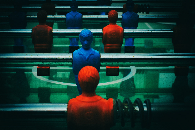 Ein buntfarbiger Tischfußballtisch mit einer Gruppe von Menschen in verschiedenenfarbigen Trikots, die in der Mitte des Tisches positioniert sind und bereit sind, ein Spiel von Tischfußball zu spielen.