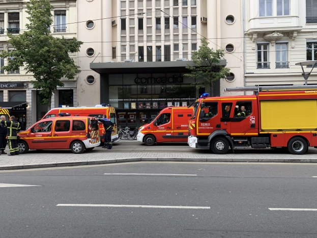 Feuerwehrfahrzeuge auf einer Straße in Paris geparkt mit Menschen in der Nähe, Gebäuden, Bäumen und einem Fahrrad im Hintergrund, wahrscheinlich nach einem Unfall.