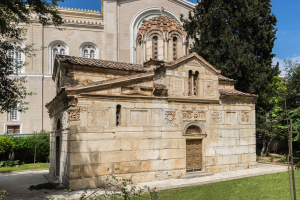 Die Kirche von St. Nikolaos in Thessaloniki, Griechenland, ein Gebäude mit Fenstern und einer Tür, umgeben von Pflanzen, Gras, einer Gruppe von Bäumen und einem bewölktem Himmel.