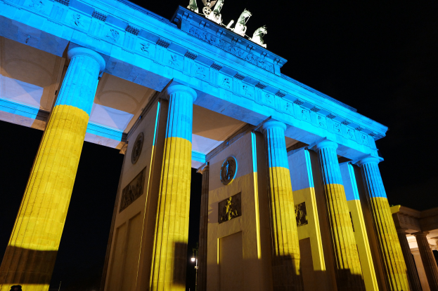 Das Brandenburger Tor in Berlin, Deutschland, erstrahlt in Blau und Gelb und steht vor einem dunklen Hintergrund mit sichtbaren Skulpturen.