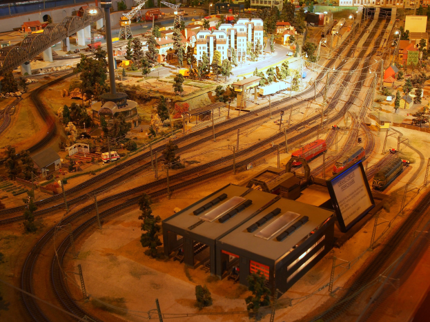 Eine detaillierte Miniatur-Modellbahnanlage in einem Museum, die Gebäude, Bäume, Eisenbahnschienen, Fahrzeuge, Masten, Lichter und andere Gegenstände zeigt, die eine belebte Stadtlandschaft nachahmen.