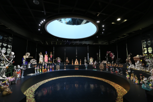 Ein großer Raum voller verschiedener Spielzeuge, darunter Skelette, die auf dem Boden angeordnet sind, mit Schädeln an den Wänden und Lichtern an der Decke, die eine festliche Stimmung für das Tag der Toten-Fest schaffen.