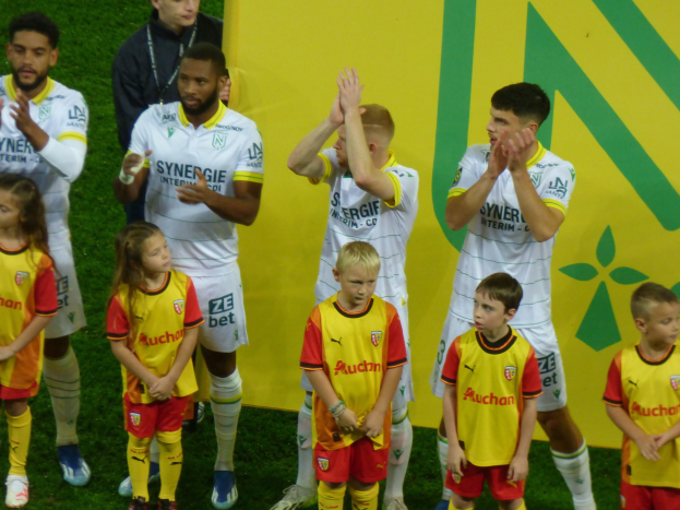 Gruppe von Füßtballspielern in Uniformen, die auf einem Ligue 1 Feld klatschen und einen Sieg feiern.