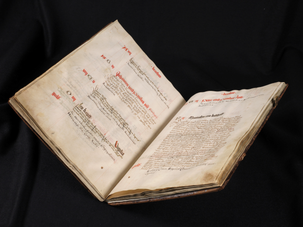 Ein offenes Buch mit rotem Text auf weißen Seiten vor schwarzem Hintergrund, das wie eine Bibel aussieht.