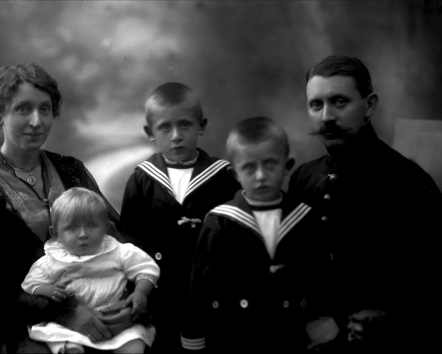 Ein Schwarz-Weiß-Foto einer Familie, die posiert, mit einer Frau, die ein Baby in den Armen hält und zwei Jungen, die neben ihr stehen, vor einem leicht unscharfen Hintergrund.