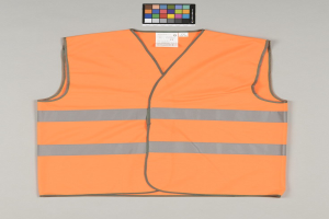 Leuchtend orangefarbene Sicherheitsweste mit reflektierenden Streifen auf einem grauen Hintergrund, mit einem angebrachten Anhänger.