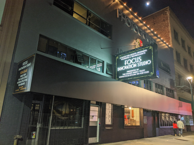 Außenansicht des Focus Innovation Studio in New York City bei Nacht, mit beleuchteten Gebäuden, Passanten auf dem Gehweg und sichtbarem Himmel.