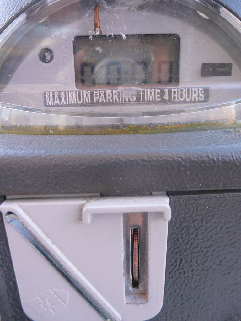 Ein Parkautomat mit der Aufschrift "Maximale Parkdauer 4 Stunden" und einem Münzschlitz mit einer Münze.