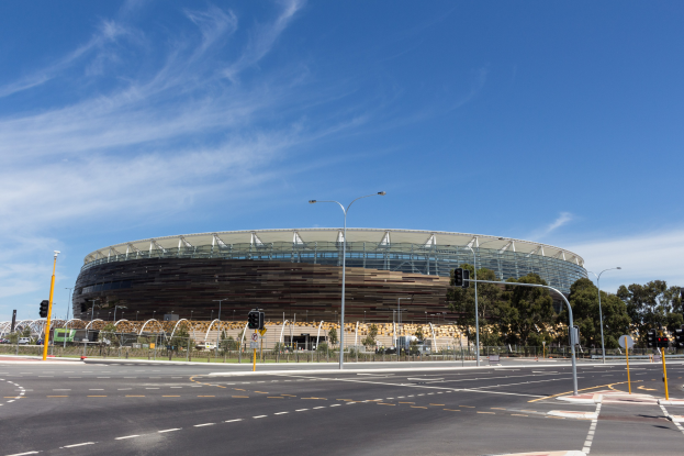 Großes Stadion mit starkem Verkehr davor, umgeben von Straßneninfrastruktur und Bäumen unter einem bewölktem Himmel.