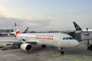 Austrian Airlines Airbus A330-300 auf dem Rollfeld am Frankfurt Airport mit Menschen, Fahrzeugen und Flughafen-Infrastruktur im Hintergrund vor einem klaren blauen Himmel.