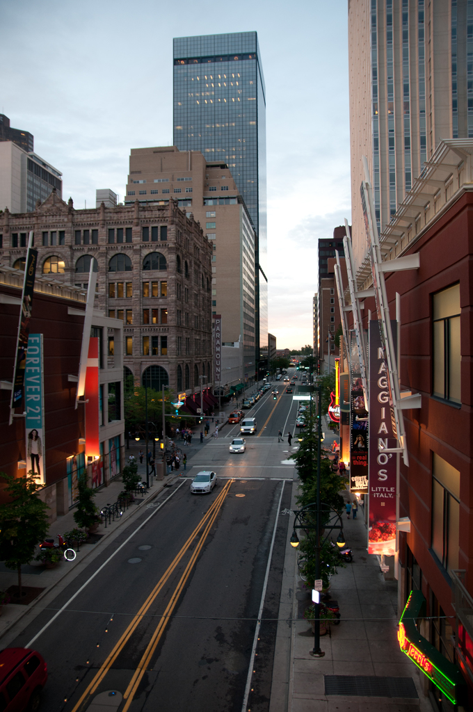 Eine Stadtansicht mit einer Straße voller Autos unten, flankiert von Gebäuden und Hochhäusern auf beiden Seiten, unter einem Himmel oben.
