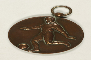 Eine bronzen Medaille in Form eines Fußballspielers mit ausgestreckten Armen und zurückgelegtem Kopf vor einem weißen Hintergrund.